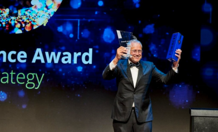 CEO holding an award and a bottle of champagne in a box on stage